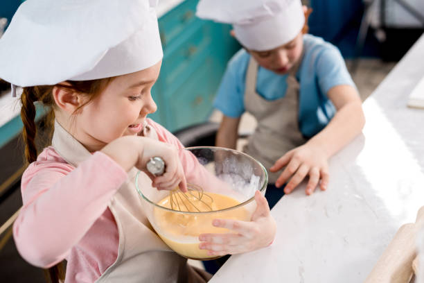 istock cute little child in chef hat making dough while brother sitting behind 917763004
