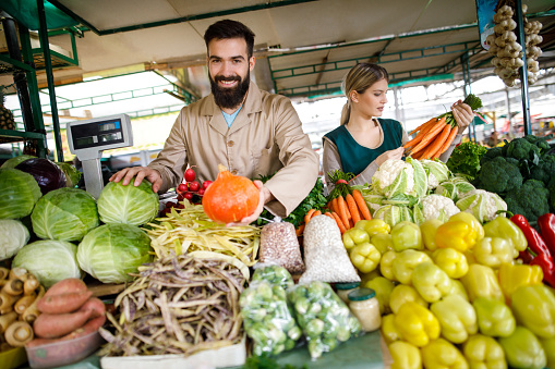 Young couple selling vegetables at farmer's food market stall.