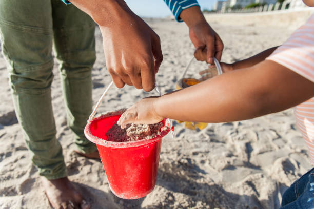 A set of colorful beach toys, including a bucket, sits in the warm sand. The bright sunlight casts soft shadows, creating a cheerful and playful summer scene.