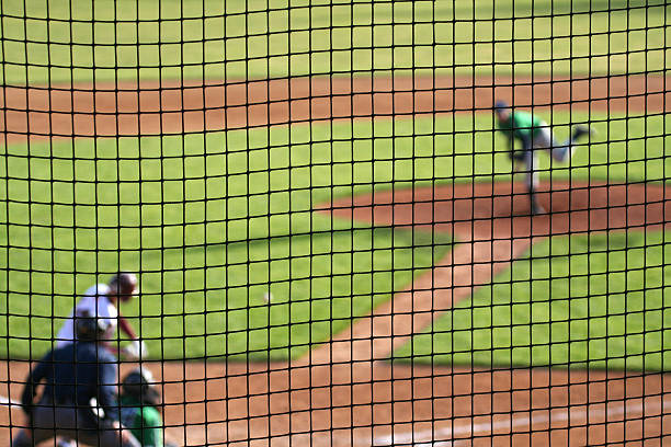 Baseball Pitch in Progress Left-handed baseball pitcher has thrown pitch to a swinging batter - with catcher and umpire waiting. Deliberate shallow depth of field with players blurred beyond a protective net screen. left handed catcher stock pictures, royalty-free photos & images