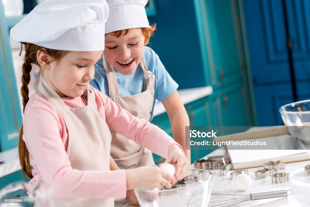 adorable heureux petits enfants en toques et tabliers, faire de la pâte ensemble dans la cuisine - Photo de Cuisiner libre de droits