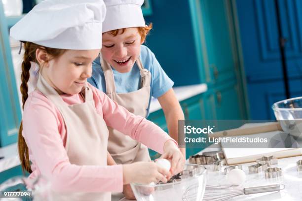 Foto de Adorável Feliz Criancinhas De Chapéu De Chef E Aventais Fazer Massa Juntos Na Cozinha e mais fotos de stock de Cozinhar