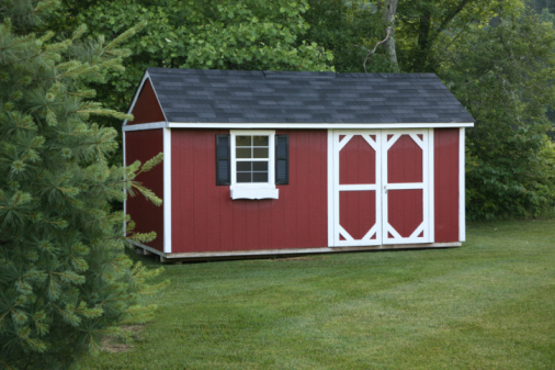 Red & white storage or potting shed set in a suburban setting surrounded by trees.
