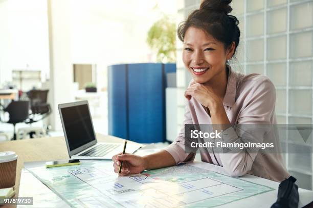 Smiling Asian Architect Working On Blueprints At An Office Desk Stock Photo - Download Image Now