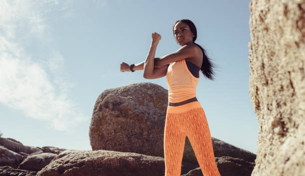Fitness woman doing hands stretching workout at the rocky beach. African female doing arms workout at the beach.