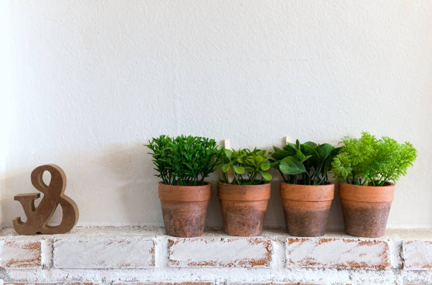 istock Four artificial plants in clay pot on wooden table with white brick wall textured background in room with copy space. 917822516