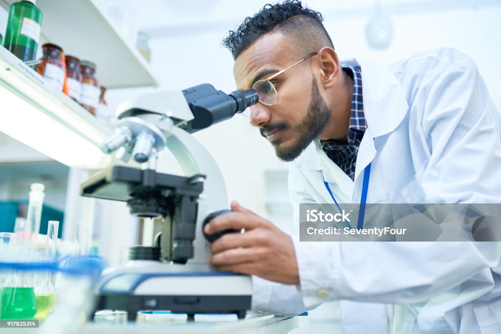 Scientist Using Microscope in Laboratory Side view portrait of young Middle-Eastern scientist looking in microscope while working on medical research in modern laboratory Laboratory Stock Photo