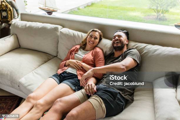 Smiling Young Couple Relaxing On Sofa Stock Photo - Download Image Now - Simple Living, Adult, Adults Only