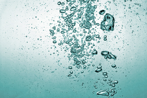 Clear water viewed through the side of an invisible surface through which blue-tinged bubbles rise toward the surface. The background is white.