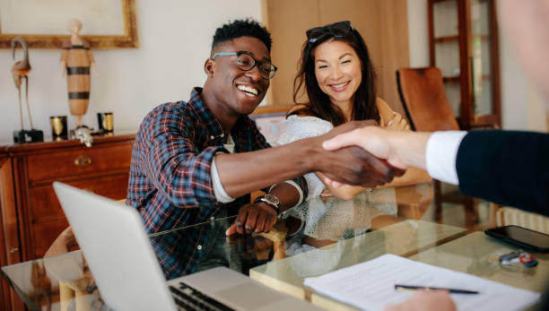Couple handshaking Real Estate Agent after signing contract Happy property owners shaking hands with real estate broker after a deal. Young couple handshaking real estate agent after signing contract. selling stock pictures, royalty-free photos & images