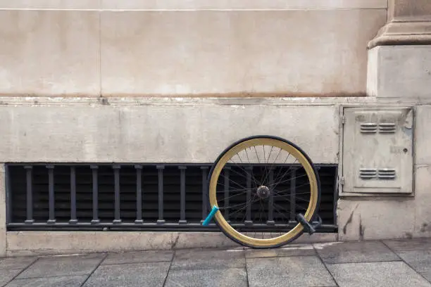 Photo of One wheel of a bicycle chained by two locks to the facade of the house, the concept of the problem of theft of bicycles in the city