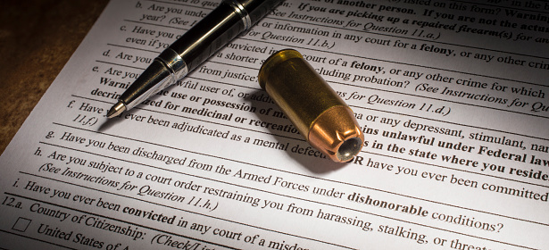 Form for a gun transfer with ammo and pen near question about dishonorable discharge