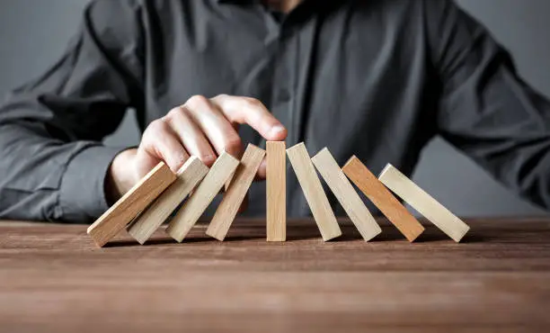 Photo of Businessman stopping domino effect with his finger. Security and insurance concept.