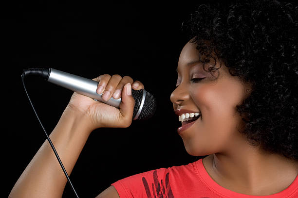 A black woman singing into a wired microphone stock photo