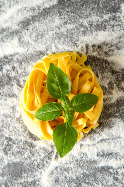 Homemade italian tagliatelle with flour and basil. Dark background.