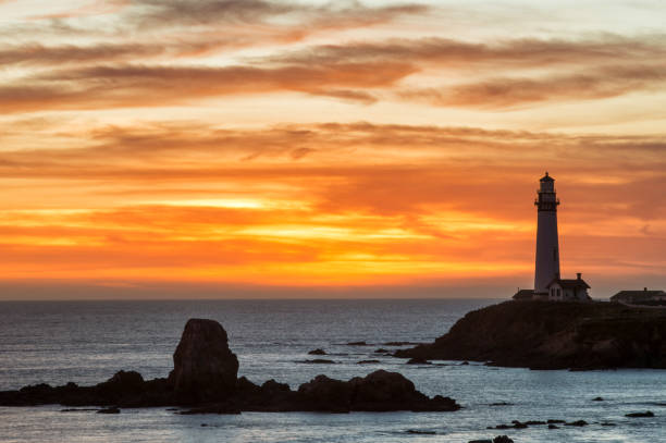 Pigeon Point Lighthouse and rocky shore silhouetted against a vibrant sunset sky.