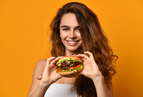 Woman eat burger sandwich with hungry mouth on yellow background. Closeup composition of Fast food concept.