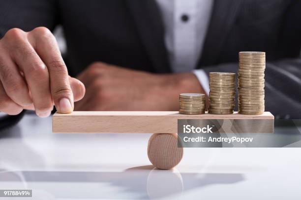 Businessperson Balancing Stacked Coins On Wooden Seesaw Stock Photo - Download Image Now