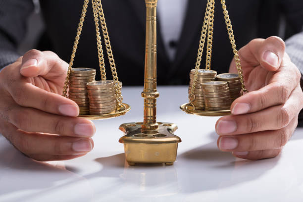 businessperson covering stacked coins on weighing scale - weight scale scale balance legal system imagens e fotografias de stock