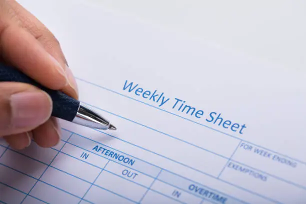 Photo of Person Filling Weekly Time Sheet With Pen