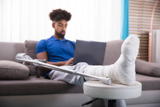 Man With Broken Leg Using Laptop Man With Broken Leg Sitting On Sofa Using Laptop orthopedic cast stock pictures, royalty-free photos & images