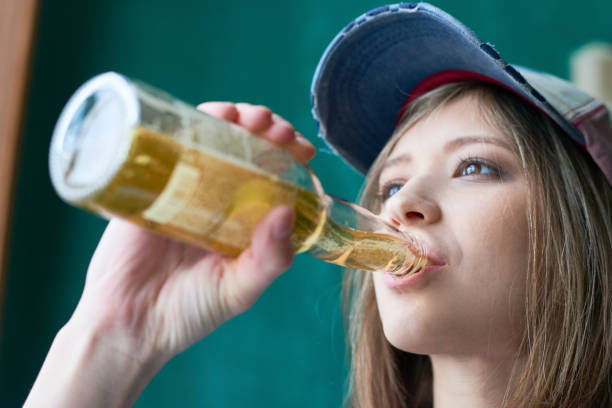 Student girl in cap drinking beer from bottle