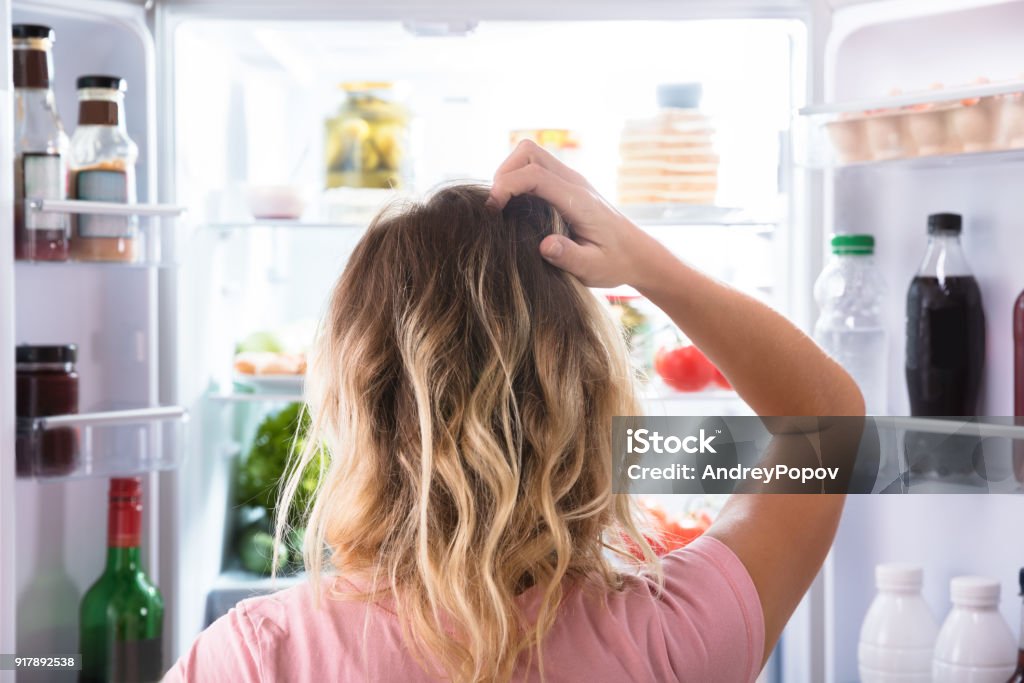 Confused Woman Looking In Open Refrigerator Rear View Of A Confused Woman Looking In Open Refrigerator At Home Refrigerator Stock Photo