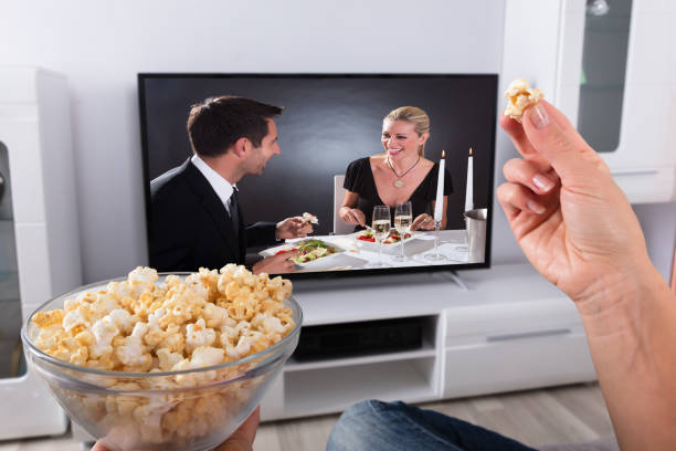 istock Person's Hand Holding Popcorn While Movie Plays On Television 917892990