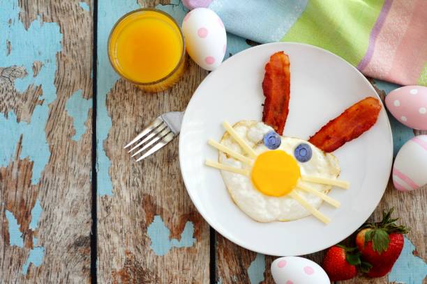 istock Easter breakfast with cute bunny face eggs and bacon. Table scene over blue wood. 917893246