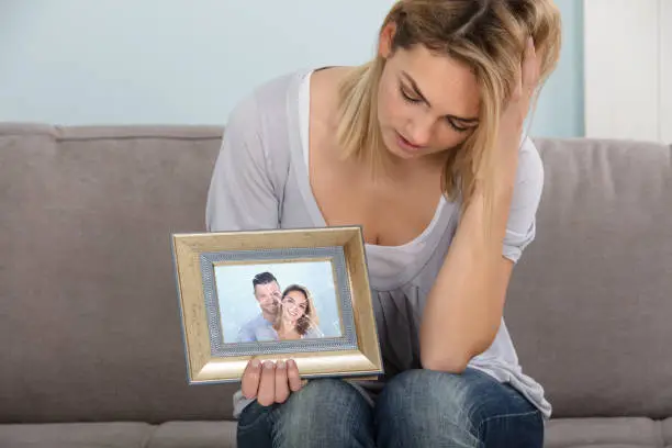 Sad Woman Holding Broken Picture Frame Of Couple In Love
