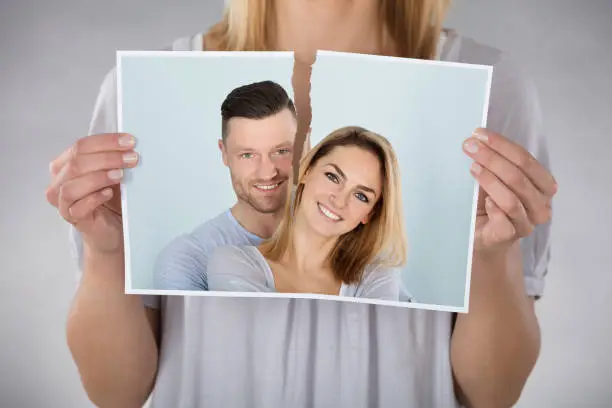 Close-up Of Woman Tearing Photo Of Smiling Couple