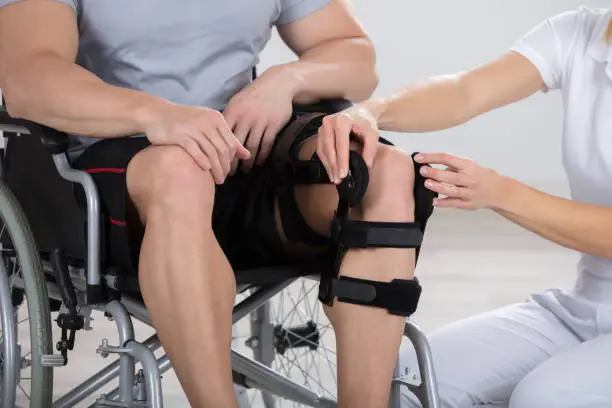 Female Physiotherapist Fixing Knee Braces On Man's Leg In A Clinic