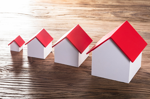 Increasing House Models With Red Roof In A Row On Wooden Table