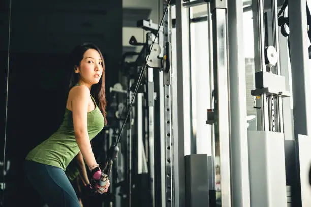 Photo of Sexy young Asian girl exercising at gym, training on pushdown cable machine, with copy space. Healthy lifestyle, sporty athletic woman, health club or fitness center advertisement concept
