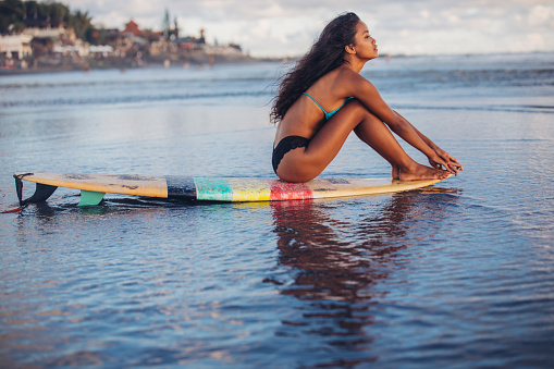 One woman, beautiful Indonesian girl sitting on a surfboard on the beach by the sea.