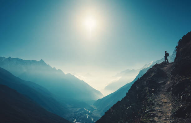 mujer de pie en la colina contra valle de montaña en día soleado. paisaje con muchacha, trail, montaña, cielo azul con sol y nubes bajas al atardecer en nepal.  estilo de vida, viajes. senderismo - mountain footpath hiking backpacker fotografías e imágenes de stock