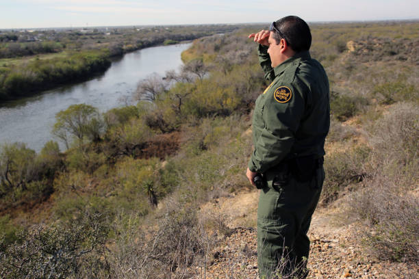 Border Patrol, Rio Grande Valley Rio Grande City, Texas, USA - January 30, 2018: A Border Patrol agent shields his eyes from the late morning sun as he looks at Mexico across the Rio Grande River in deep south Texas. This stretch of the river has recently seen an upsurge in crossings, both of people and marijuana. jeff goulden border security stock pictures, royalty-free photos & images