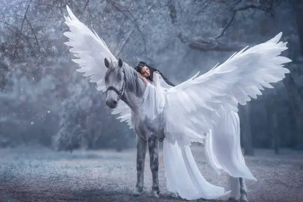 Beautiful, young elf, walking with a unicorn. She is wearing an incredible light, white dress. The girl lies on the horse. Sleeping Beauty. Artistic Photo