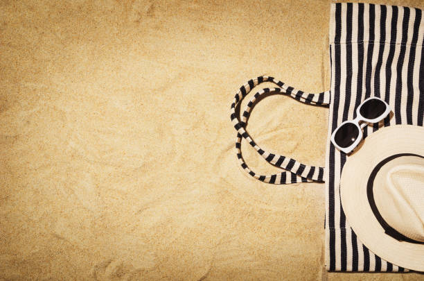 Top view of sandy beach with towel frame and summer accessories. Background with copy space and visible sand texture. Border composition made of towel