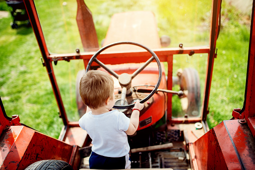 Baby boy holding a steering wheel of tractor. Growing up at a countryside.