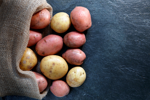 Red and Gold potatoes in hessian sack on slate table top with copy space