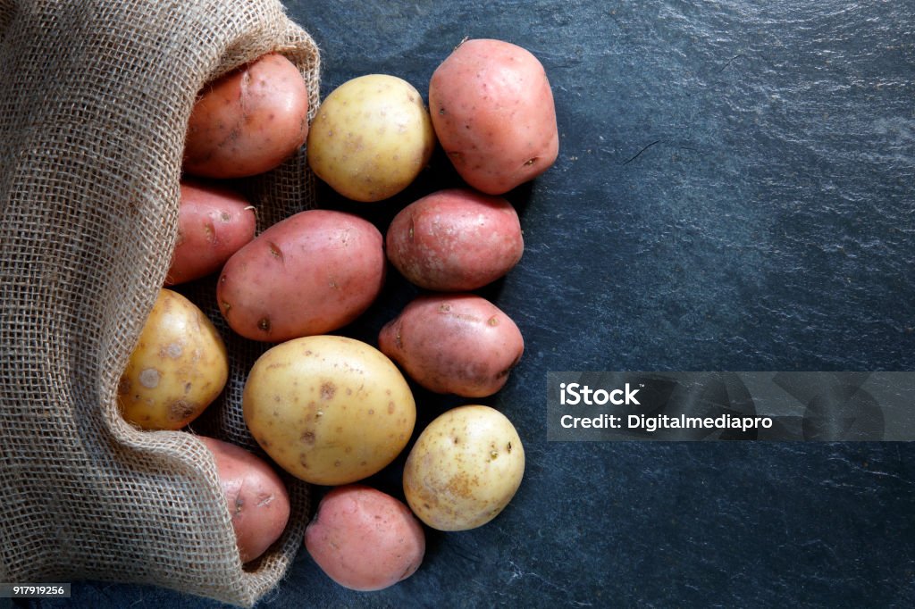 Red and Gold potatoes in hessian sack Red and Gold potatoes in hessian sack on slate table top with copy space Raw Potato Stock Photo