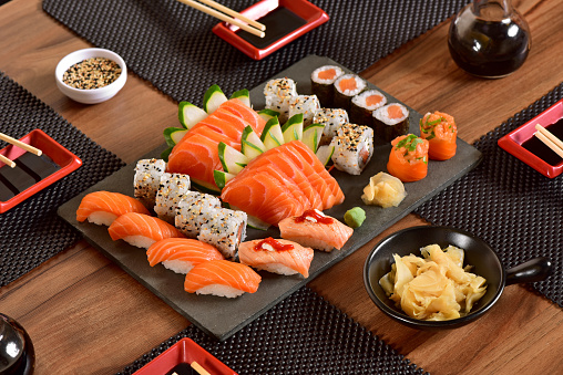 A woman hand wields chopsticks to delicately place fresh salmon sashimi on a plate in a Japanese restaurant, capturing the art of dining.