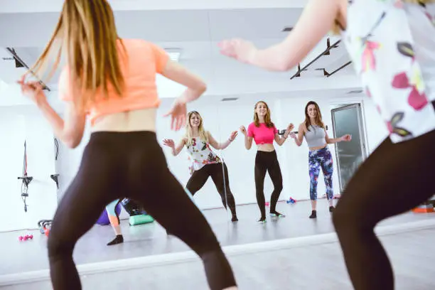 Photo of Group of Cute Smiling Females Training Zumba in front of the Mirror in Gym