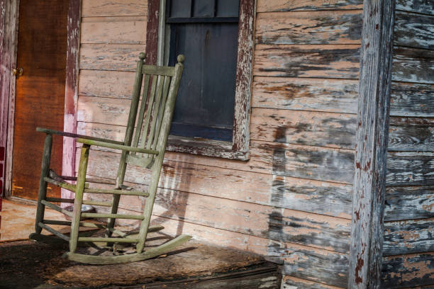 A vintage green rocking chair in a rural setting on the front porch of an old farmhouse.