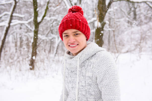 портрет милого мальчика в красной вязаной шляпе на открытом воздухе - winter clothing hat human eye стоковые фото и изображения