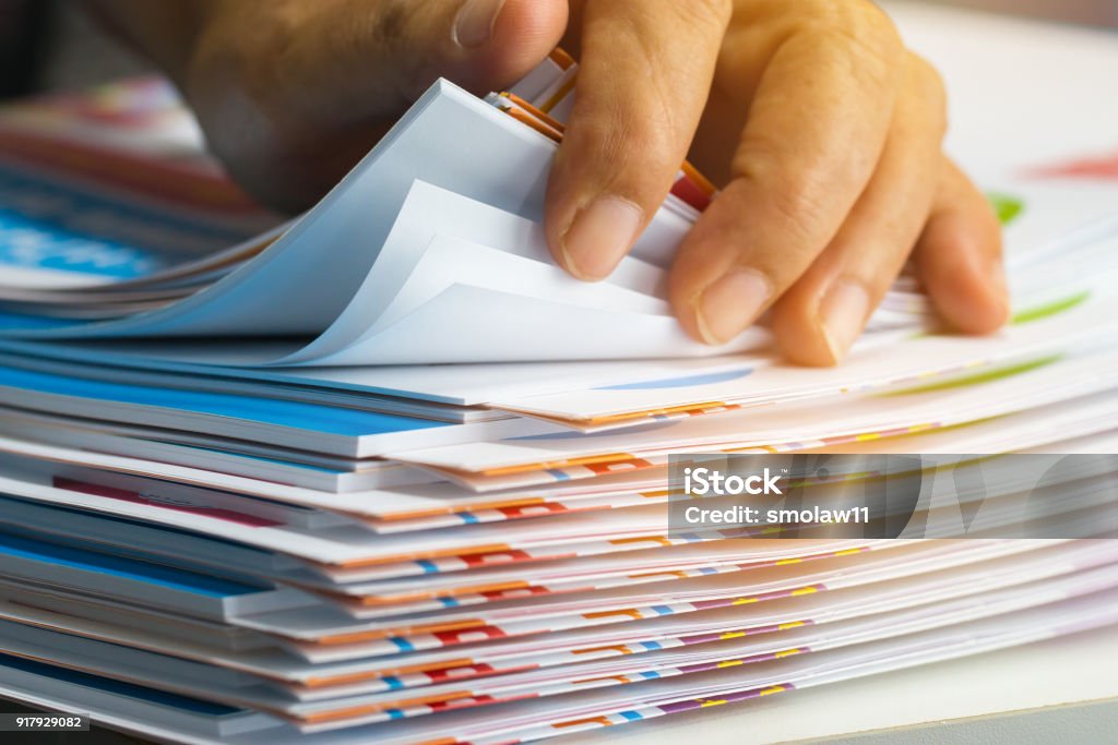 Businessman hands searching unfinished documents stacks of paper files on office desk for report papers, piles of sheet achieves with clips on table, Document is written, drawn,presented. Document Stock Photo