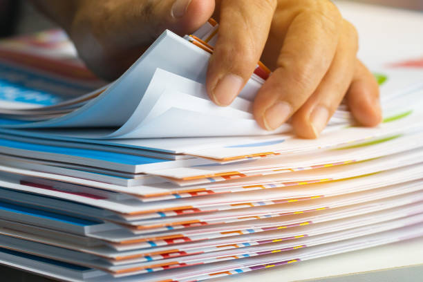Businessman hands searching unfinished documents stacks of paper files on office desk for report papers, piles of sheet achieves with clips on table, Document is written, drawn,presented. stock photo