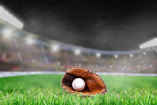Baseball glove and ball on grass in brightly lit outdoor stadium. Focus on foreground and shallow depth of field on background with copy space. Fictitious background stadium created entirely in Photoshop.