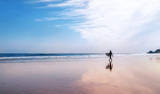 Surfer with surfboard walks on coast line
